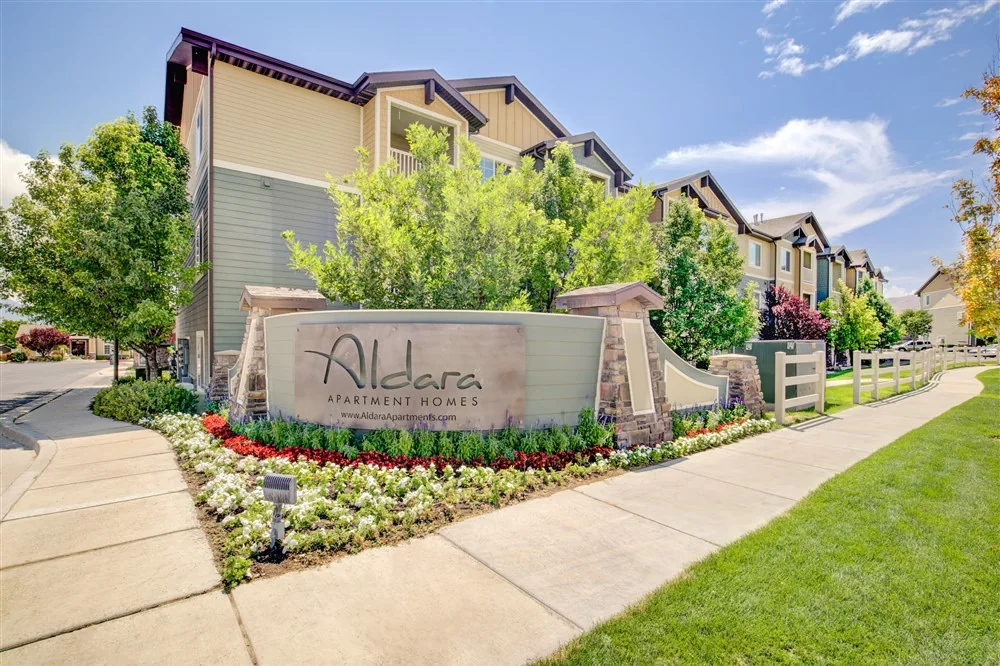 Aldara Apartment Homes entrance framed by mature trees and flowering landscaping